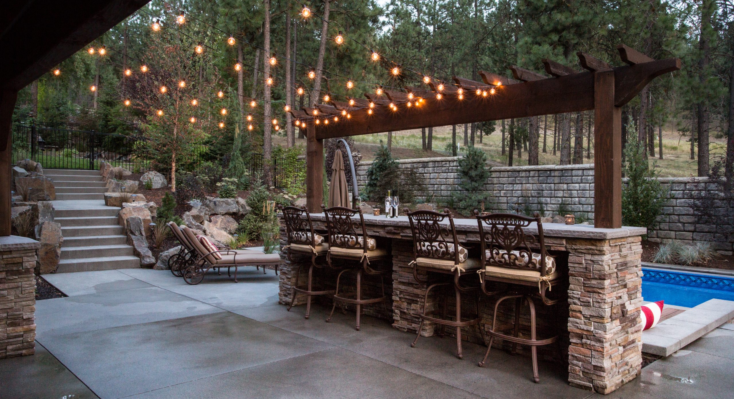 an arbor with a bar and party lights overlooking pool